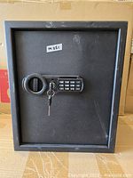 Front view of black electronic safe showing keypad, rotary knob, and key inserted