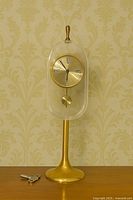Full view of brass pedestal clock under clear acrylic dome with key visible