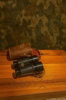 Binoculars beside leather case on wood surface
