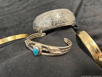 Four bracelets arranged on black fabric: wide etched bangle, two thin bangles, turquoise stone cuff