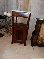 Front view of dark wood telephone stand showing marble top, drawer, turned supports, and lower cabinet