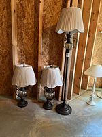 Floor lamp and two table lamps with shades displayed together against unfinished wall