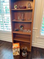 Full bookshelf view with crystal bowls, vases, porcelain flowers, boxed item and floor vase