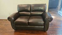 Front view of dark brown faux leather loveseat showing nailhead trim and overall condition