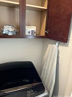 Shark iron wrapped in plastic, Sunbeam travel iron/steamer box, ironing board leaning against wall