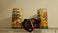 Two Lincoln Logs containers and fabric bag with wooden train parts on shelf