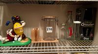 Shelf view showing M&M's figurine, clear canister, wooden holder, various glass bottles and boxed growler
