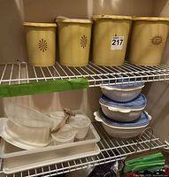 Four harvest gold canisters, three white/blue bowls, rectangular container, condiment cups on wire shelf