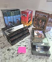Four different VHS box sets are arranged on a countertop. Visible titles include The Invaders, No Price Too High, Spartacus, along with others in the background.