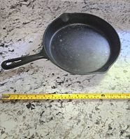 Top view of cast iron pan with measuring tape showing approx. 12 inch diameter.