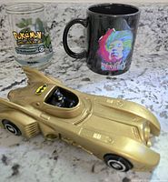 Lot of three collectible items on countertop: Hendrix mug, Batman car, and Pokémon glass