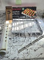 Metal kabob rack with packaging in background, white plastic dry line launch reel and metal curtain rod bracket.