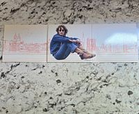 Folded outer cover art showing John Lennon sitting with city skyline background in red line art