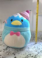 Front view of large blue penguin plush toy with cupcake hat and measuring tape showing height approximately 19 inches.