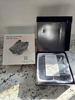 Open box showing the quadcopter drone, controller, and instruction manual inside the packaging, placed on a countertop.