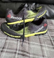 Side profile of men's black and yellow Reebok running shoe showing branding and sole detail.