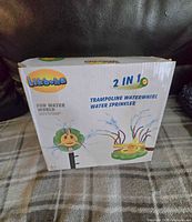 Box front showing Likboha 2-in-1 trampoline waterwhirl and water sprinkler with cartoon flower design in green and yellow.