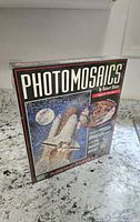 Front angled view of the sealed Photomosaics Space Shuttle puzzle box showing the mosaic image of the shuttle and astronaut.