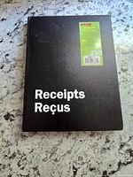 Front black cover of the receipt book with 'Receipts Reçus' in white text and green Staples label