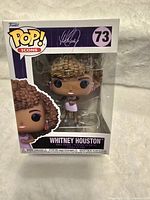 Front view of Whitney Houston Funko Pop! figure in original box showing figure with curly hair and purple dress, box number 73