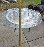Side view of round glass patio table with tape measure showing height around 21 inches.