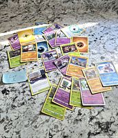 Multiple assorted Pokemon trading cards laid out, showing various types, energies, and characters.