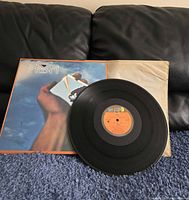 Full view of PRISM vinyl record with cover and inner sleeve placed on blue carpet and black couch background.