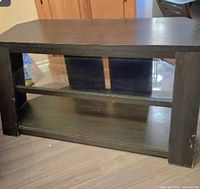 Front view of black wooden TV entertainment unit showing top surface and one glass shelf in middle with lower wooden shelf.