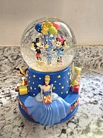 Front view of water globe showing Mickey and Minnie holding balloons inside the globe, with Cinderella figurine on the base front.