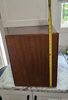 Side view of wooden cajon with measuring tape showing height approximately 12 inches.