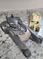 Two Batman toy vehicles on countertop, black and tan camouflage design