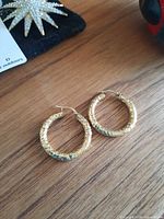 Pair of hammered yellow gold hoop earrings on wood surface