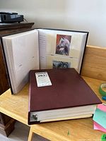 Two burgundy binder photo albums, one open showing plastic sleeves with prints