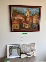 Framed oil painting above two unframed artworks