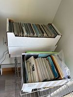 Two document boxes and one smaller box filled with upright postcards on shelf