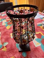 Full view of the decorative metal frame holding multicolored glass beads and the metal base on a decorative tablecloth.