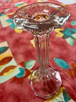 Close-up image of one clear crystal candle holder showing scalloped edge top and hexagonal stem and base.