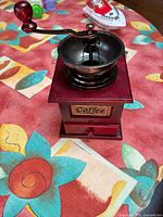 Front view of manual coffee grinder with metal crank and wooden base on colorful cloth