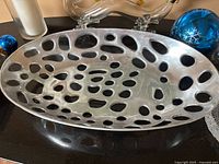 Top down view of the oval decorative metal bowl showing the perforated holes pattern and metallic finish.
