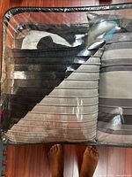 View of black ribbed bed cover and multiple decorative pillows inside clear plastic storage bag