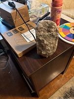 Front view photo of a small grayish-white rock salt lamp on a dark wooden table, with surrounding household items visible but not part of the lot.