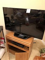 47 inch LG TV displayed on wooden TV stand with Panasonic VHS player in shelf below and remote controls on TV stand.