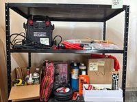 Full shelf view showing Cen-Tech power pack, jumper cables, various automotive fluids, windshield wipers, lug nuts, air compressor hoses, blankets, and other car maintenance items.