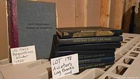 Stack of seven aviators flight log books with dark covers and gold embossed titles, beside a gray 1920 US Navy regulations binder on a plastic shelving unit.