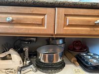 Kitchen counter photo showing mixing bowl on stand mixer base, metal baking pans, muffin tins, rolling pin, and pie plates under wooden cabinets.