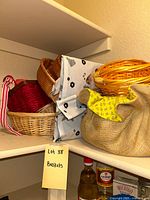Various baskets stacked together on a pantry shelf, showcasing different sizes and colors including red, natural wicker, and yellow fabric-covered basket.