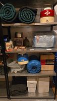Shelf with rolled green sleeping mats, Coleman water jug, vintage camping items including cookware and a propane lantern box.