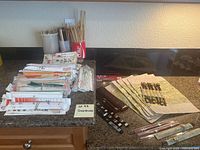 Overview of lot showing multiple bundles of disposable chopsticks, cups holding more chopsticks, and six fabric placemats with matching chopsticks arranged on countertop.