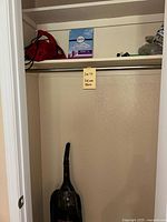 Wide view of the closet with the handheld Dirt Devil vacuum, vacuum bags and parts on the shelf above, and the Hoover WindTunnel vacuum on the floor.