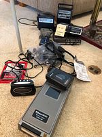 Wide view of the lot showing the Timex clock radio, Sony Walkman, B.V. Service electronic VHS player, radios, cables and accessories laid on carpet.